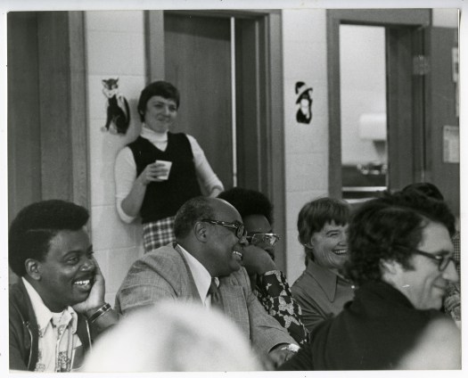 A group of Black and white people smiling and laughing. They appear to be attending a meeting.